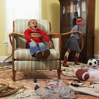 Young boy and girl (6-7 years) playing in messy living room, girl tying boy with rope