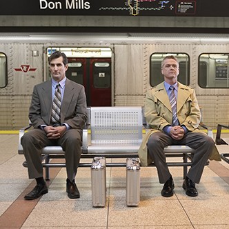 Two identical briefcases in front of two men sitting on bench in subway platform