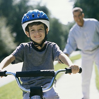 Boy cycling with his father standing behind him