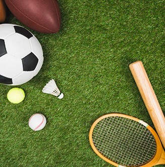 top view of various sport balls, baseball bat and glove, badminton racket on green lawn