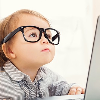 Smart toddler girl wearing big glasses while using her laptop