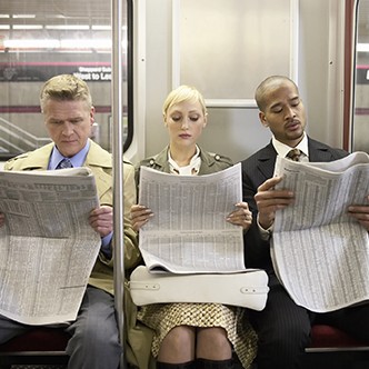 Two men and woman sitting in subway train side by side, reading newspaper